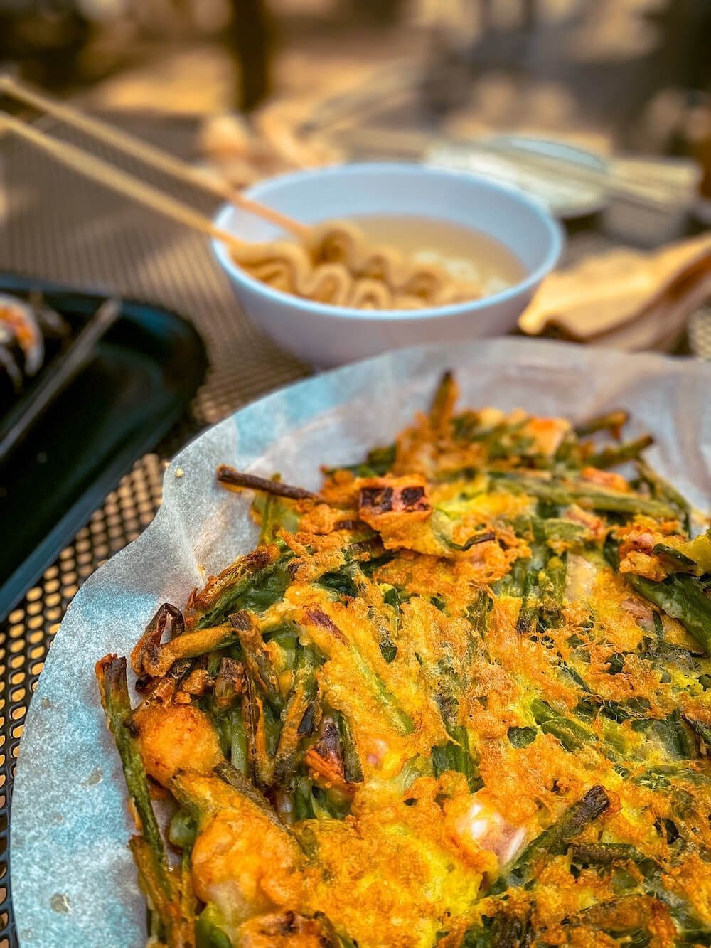 Close-up of a crispy golden Korean seafood haemul pajeon pancake served with a bowl of warm fish cake odeng soup at Hwadamsup