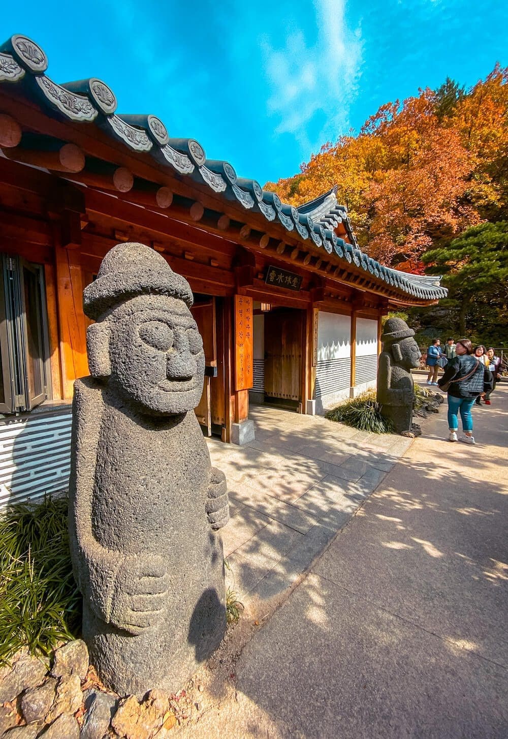 Stone Dol Hareubang statues guarding a traditional Korean tiled roof entrance gate at Hwadam Botanic Garden
