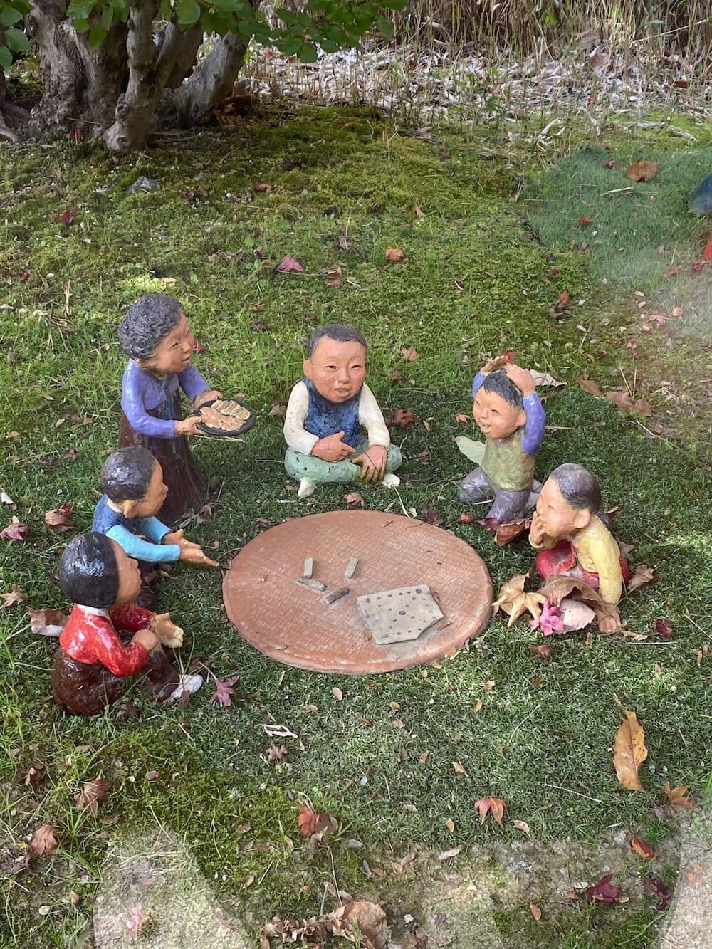 Small traditional Korean clay figures depicting village life sitting in a circle on a green mossy patch at Hwadam Botanic Garden